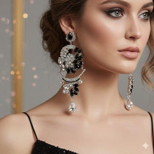 May include: Elegant chandelier earrings with a silver-tone metal setting. The earrings feature a combination of clear and black crystals in a floral and teardrop design. The earrings are a statement piece.