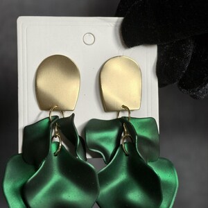 Op de afbeelding: Een paar goudkleurige, rechthoekige oorbellen met een matte afwerking. Daaronder hangen drie gelaagde, bloemblad-vormige, smaragdgroene oorbellen aan goudkleurige ringen. De oorbellen worden gepresenteerd op een witte kaart.