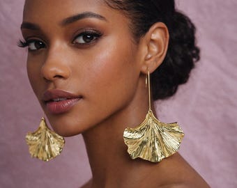 May include: Gold-colored, fan-shaped earrings with a textured surface. The earrings hang from a thin, straight wire. The earrings are a statement piece, adding a touch of elegance and sophistication.