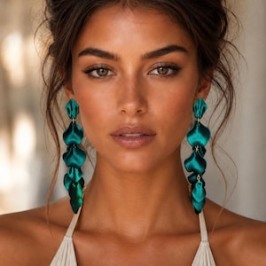 May include: A pair of long, dangling earrings featuring a series of layered, petal-shaped components in a deep, vibrant emerald green color. The earrings have a smooth, satin-like finish and are connected by small, thin metal links in a vertical arrangement.