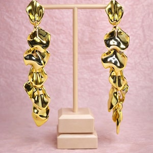 Pair of hand-assembled gold leaf drop earrings on a jewelry stand, showcasing the intricate hammered texture and golden shine.