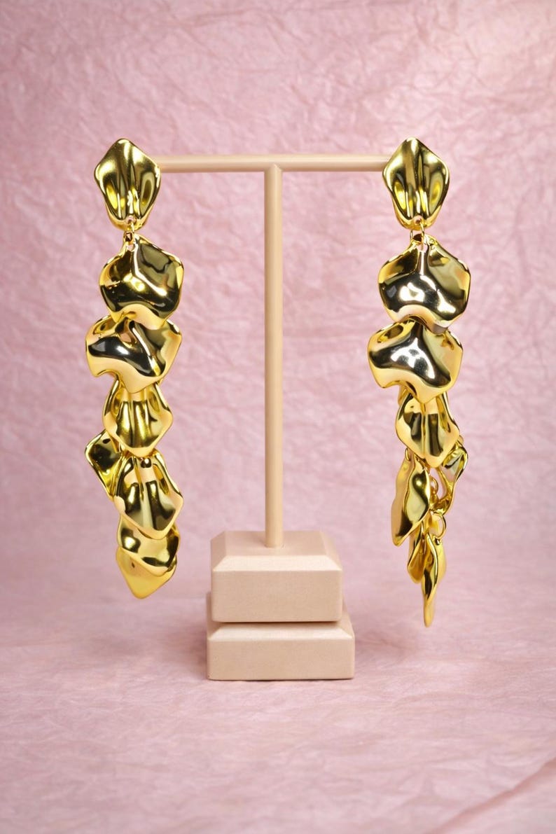 Pair of hand-assembled gold leaf drop earrings on a jewelry stand, showcasing the intricate hammered texture and golden shine.