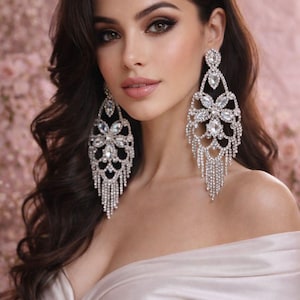 May include: Elegant, chandelier-style earrings with a floral design and dangling crystals. The earrings are silver-toned and sparkle, adding a touch of glamour. The earrings are a statement piece, perfect for special occasions.