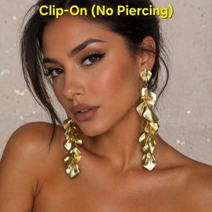 May include: Gold clip-on earrings with a cascading leaf design. The earrings are long and dangle, featuring multiple layers of gold-coloured metal leaves. The text "Clip-On (No Piercing)" is visible at the top of the image.