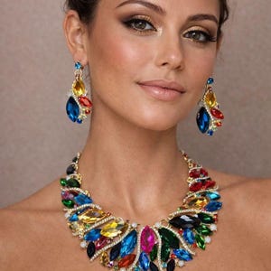 May include: A colorful statement necklace and matching earrings. The jewelry features a gold-toned setting and is adorned with a variety of vibrant, faceted gemstones in shades of blue, yellow, red, green, and pink. The earrings dangle elegantly.
