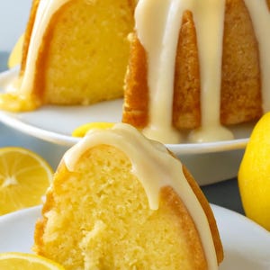 May include: A slice of lemon cake with white icing, served on a white plate with lemon slices. The cake is a golden yellow color, and the icing is dripping down the sides. The cake is a bundt cake shape.