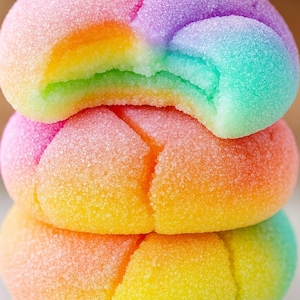 May include: A stack of rainbow-coloured cookies. Each cookie is a different colour, with a sugary coating. One cookie has a bite taken out of it, revealing the layers of colour inside.