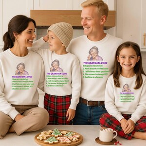 Puede incluir: Una familia de cuatro personas con sudaderas blancas a juego. Cada sudadera presenta un gráfico de una abuela y el texto "THE GRANDMA CODE" con una lista de reglas. La familia sonríe y está reunida en un entorno de cocina.