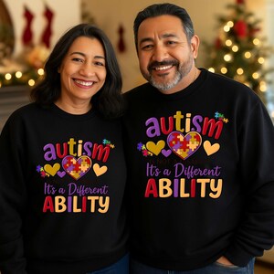 May include: Two people wearing black sweatshirts with the word "autism" in purple and red, and the phrase "It's a Different Ability" in colorful letters. The design includes a puzzle heart and yellow hearts.