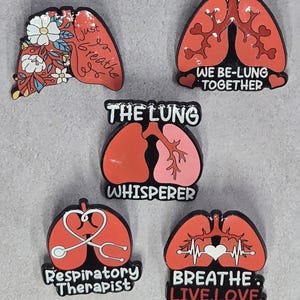 May include: Five red and black lung-shaped pins with various designs and text. One pin has flowers and the words "Just Breathe." Another says "We Be-Lung Together." Other pins say "The Lung Whisperer," "Respiratory Therapist," and "Breathe. Live. Love."