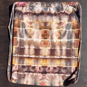 Könnte beinhalten: Ein Kordelzug-Rucksack mit Batikmuster in Braun-, Orange- und Grautönen. Die Tasche hat horizontale Streifen und einen Kordelzugverschluss. Der Stoff hat ein strukturiertes Aussehen, und der Kordelzug ist hellbeige.