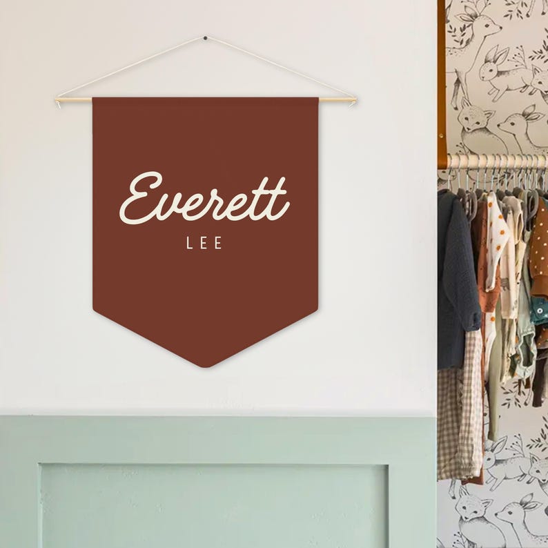 Pode incluir: Uma faixa marrom com o nome "Everett" em letras brancas e cursivas, e a palavra "LEE" abaixo. A faixa &eacute; suspensa de uma haste de madeira com um cord&atilde;o branco. A faixa est&aacute; pendurada em uma parede branca.