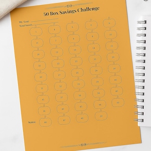 Può includere: Un foglio di carta arancione con un design "50 Box Savings Challenge". La carta ha una griglia di caselle a forma di zucca numerate da 1 a 50 per tenere traccia dei risparmi. Include spazio per obiettivi e note.