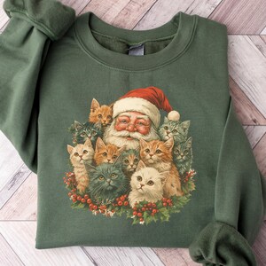 May include: Green sweatshirt featuring a vintage-style graphic of Santa Claus surrounded by several cats. Santa wears a red hat, and the cats have various fur colors. The sweatshirt has long sleeves and a crew neck, perfect for the holiday season.