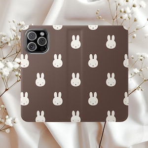 May include: A brown phone case with a repeating pattern of white bunny faces. The case is rectangular with rounded corners and a camera cutout. The case is designed to protect a phone and has a smooth texture.