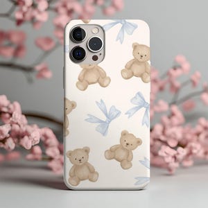 May include: A white smartphone case featuring a repeating pattern of light brown teddy bears and light blue bows. The design is distributed across the back of the case, which includes a cutout for the camera lenses on the upper left side.