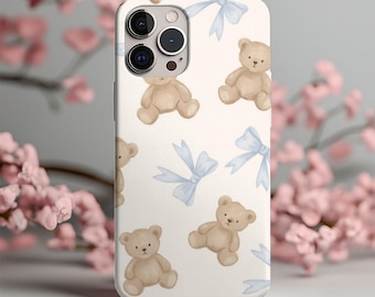 May include: A white smartphone case featuring a repeating pattern of light brown teddy bears and light blue bows. The design is distributed across the back of the case, which includes a cutout for the camera lenses on the upper left side.