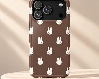May include: A brown smartphone case featuring a repeating pattern of small white rabbit faces. The case has a black camera cutout area with three circular lenses and a flash, designed to fit a modern mobile device with a sleek finish.