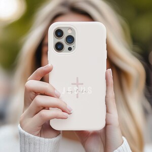May include: A light pink phone case with a cross and the words "Jesus my life" in a script font. The phone case has a camera cutout and is held up in front of a person.