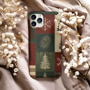 May include: A rectangular smartphone case featuring a patchwork design of dark green and deep red squares. The pattern includes white line-art illustrations of pine trees, snowflakes, and starbursts, with a triple-lens camera cutout at the top.