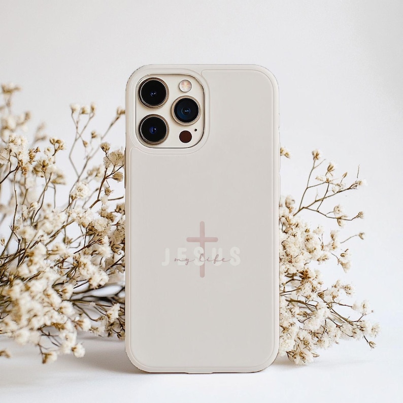 May include: A light beige phone case with a cross and the words "Jesus my life" in a script font. The phone case has a camera cutout and is surrounded by white flowers.