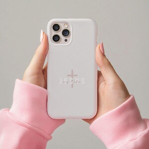 May include: A white phone case with the words "JESUS my life" and a cross graphic in a soft pink color. The phone case is held by hands wearing a pink sweatshirt.