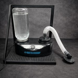 May include: A black humidifier with a clear water reservoir and a white flexible tube. The device has a black base with a perforated surface and a metal frame. The text "REPTI FOGGER" is visible on the front.