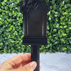May include: A black gothic-style garden stake with an arched top and decorative details. The stake has a rectangular body and a pointed bottom for easy insertion into the ground. The stake is made of a solid black material.
