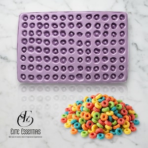 May include: A lilac silicone mould with many small, round cavities is positioned above a pile of colourful, ring-shaped cereal. The cereal is a mix of red, orange, yellow, green, and blue. The Elite Essentials logo is in the bottom left corner.