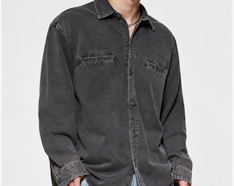 May include: A long-sleeve button-down shirt in a faded charcoal gray denim fabric. The shirt features a classic collar, a full-length front button placket, and two horizontal chest pockets with flaps. The material has a washed, worn-in appearance.