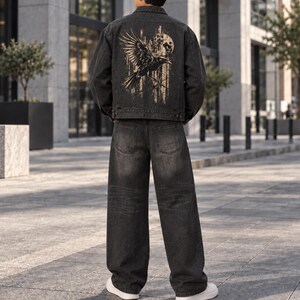 May include: A charcoal gray denim jacket featuring a large graphic print on the back of a black crow in flight against a full moon, paired with matching charcoal gray denim jeans and white sneakers, viewed from the back in an outdoor setting.