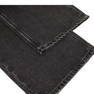 May include: A pair of charcoal black denim jeans featuring a straight leg cut with visible stitching along the hems and side seams. The fabric has a slightly faded, washed-out texture throughout, showcasing the classic weave of the cotton denim material.