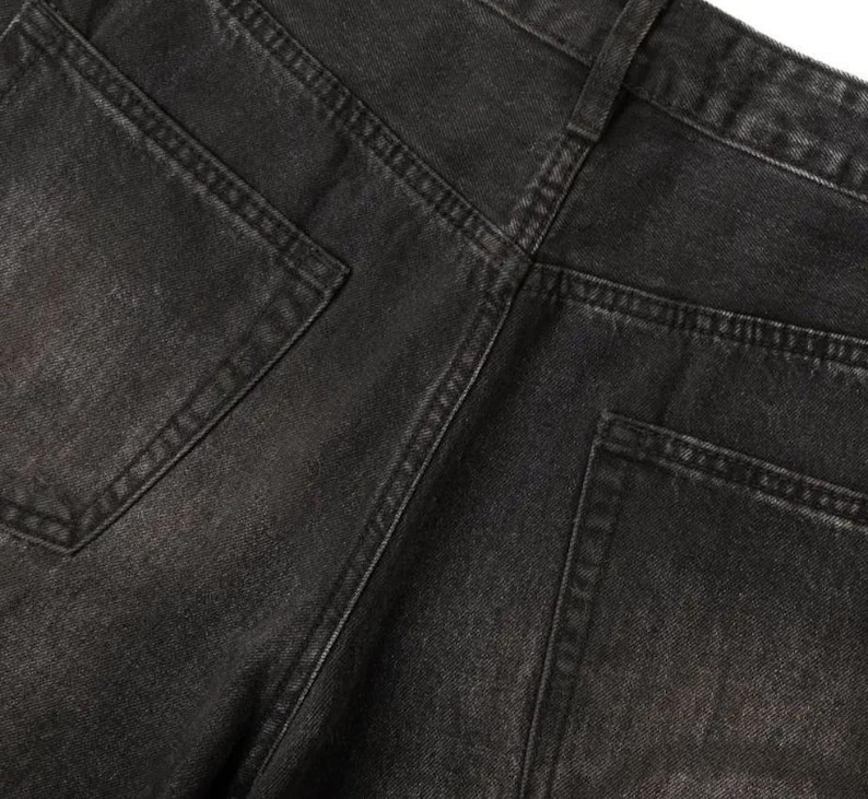 May include: A pair of black denim jeans featuring a faded wash, a high-rise waistband with belt loops, and two back pockets. The fabric displays a textured weave with visible stitching along the seams and pockets, showcasing a classic five-pocket construction.