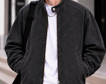 May include: A charcoal grey denim bomber jacket featuring a stand-up collar with a single snap button closure, a full-length metal zipper, and two side pockets. The jacket is worn over a plain white t-shirt and includes a black shoulder strap.