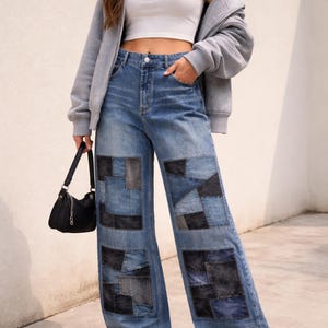 Könnte beinhalten: Hellblaue Jeans mit Denim-Patchwork und weitem Bein. Die Jeans haben dunkle Denim-Patches. Das Model trägt ein weißes Crop-Top, einen grauen Kapuzenpullover und weiße Turnschuhe. Eine schwarze Handtasche mit Kettenriemen ist ebenfalls zu sehen.