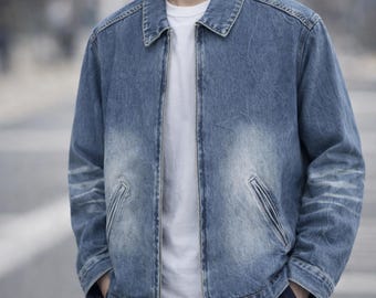 May include: A blue denim jacket with a faded wash, featuring a classic collar, a full-length silver metal zipper closure, and two slanted welt pockets at the waist. The jacket is worn over a plain white t-shirt and dark-colored trousers.