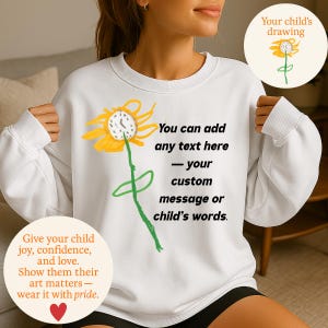 Peut inclure: Sweat-shirt blanc avec un dessin d'enfant représentant un tournesol jaune et une tige verte. Le texte "You can add any text here - your custom message or child's words" est imprimé sur le devant. Le texte supplémentaire dit "Give your child joy, confidence, and love."