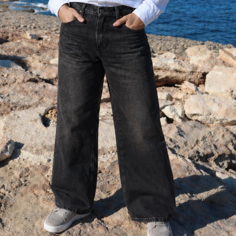 May include: High-waisted wide-leg jeans in a faded black denim wash. These pants feature a classic five-pocket design, a button and zipper fly closure, and belt loops at the waistband. The denim has a slightly distressed, worn-in appearance.