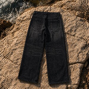 May include: A pair of black denim jeans with a faded wash, featuring a high-waisted design, a straight-leg cut, two back patch pockets, a waistband with belt loops, and visible stitching along the seams and hems, shown from the back view.