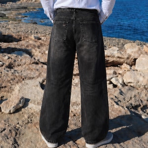 May include: A pair of loose-fitting, high-waisted black denim jeans with a faded wash. The jeans feature a classic five-pocket design, including two back pockets with visible stitching, a waistband with belt loops, and a straight-leg silhouette.