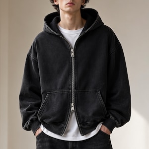 May include: Black zip-up hoodie with a drawstring hood and front pockets. The hoodie has a silver zipper and is worn over a white t-shirt. The garment has a slightly faded appearance.