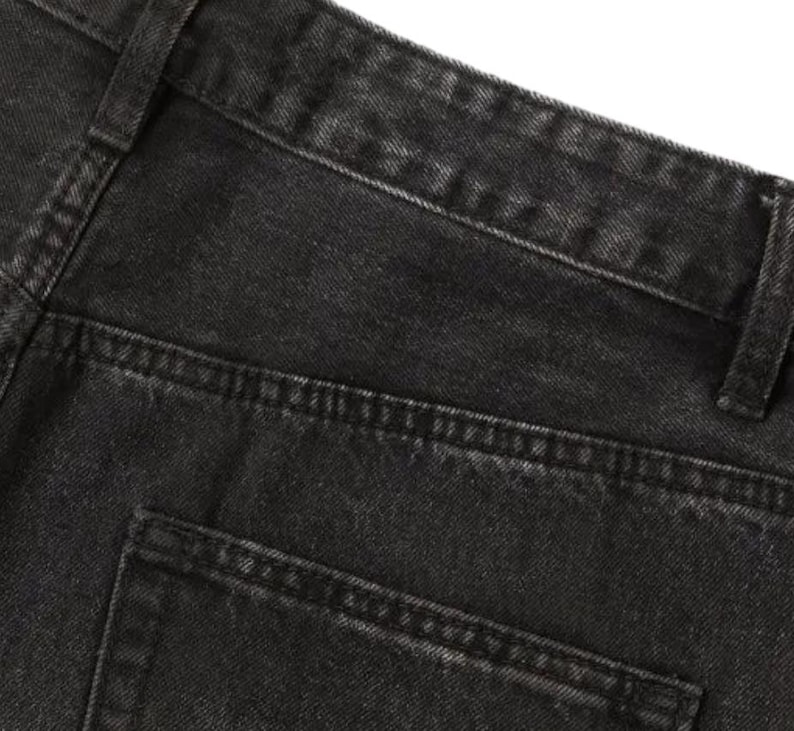 May include: A pair of black denim jeans featuring a high-waisted design with a structured waistband, belt loops, and a visible back pocket. The fabric has a washed-out, charcoal-toned texture with reinforced stitching along the seams and pockets.