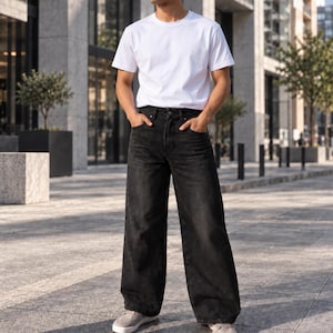 May include: A plain white short-sleeved crew neck t-shirt paired with loose-fitting black denim jeans. The jeans feature a high-waisted design with a button fly, front pockets, and a wide-leg silhouette that extends down to light gray sneakers.