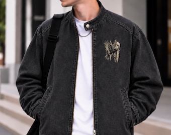 May include: A charcoal grey denim bomber jacket featuring a stand-up collar with a snap button closure, a full-length front zipper, and a graphic print on the left chest depicting a flying crow against a circular moon and vertical lines.
