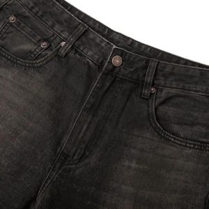 May include: A pair of black denim jeans featuring a faded wash, a button fly closure, and copper-toned metal rivets. The garment includes a standard five-pocket design with a coin pocket on the right side and belt loops along the waistband.