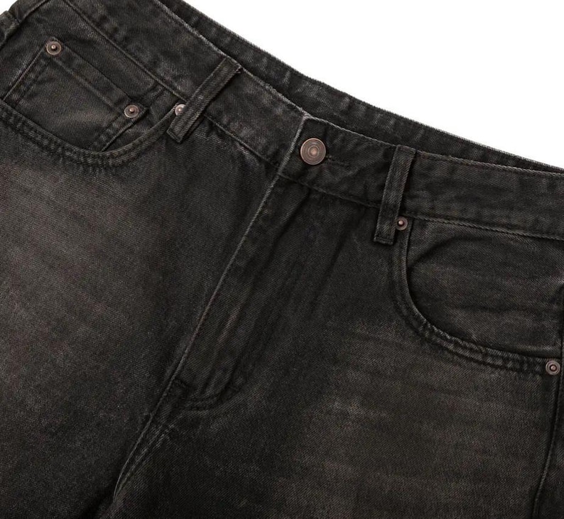 May include: A pair of black denim jeans featuring a faded wash, a button fly closure, and copper-toned metal rivets. The garment includes a standard five-pocket design with a coin pocket on the right side and belt loops along the waistband.
