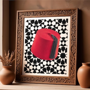 May include: A framed print featuring a red fez hat with a black tassel against a black and white geometric pattern. The frame is made of carved wood and is displayed on a wooden surface with two terracotta vases.