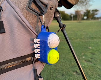 May include: A blue golf ball and tee holder attached to a golf bag. The holder contains a white golf ball, a yellow golf ball, and several white golf tees. The holder is attached to the bag with a black carabiner.