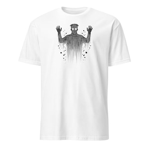 Peut inclure: T-shirt blanc avec un motif noir représentant une silhouette avec les mains levées et des yeux brillants. La silhouette est composée de lignes verticales et de détails pixélisés, avec une couronne sur la tête.