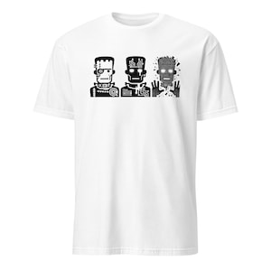 Könnte beinhalten: Weißes T-Shirt mit einer schwarzen Grafik von drei roboterartigen Figuren. Die Figuren haben unterschiedliche Designs, eine erinnert an Frankensteins Monster. Die Grafik ist mittig platziert und bietet ein auffälliges, aufmerksamkeitsstarkes Design.